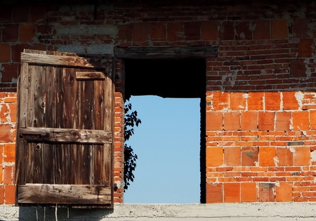 A brick wall with an old ruined wooden door open on the skyの写真素材
