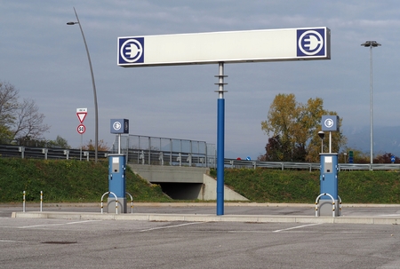 Electric car charging station with a large blank road sign over the refueling pointsの写真素材
