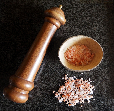 Himalayan pink salt with wooden grinder on black marble tableの写真素材