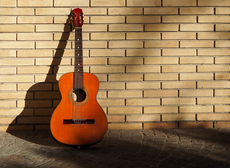 Classical guitar on a sidewalk and resting on a yellow brick wallの写真素材
