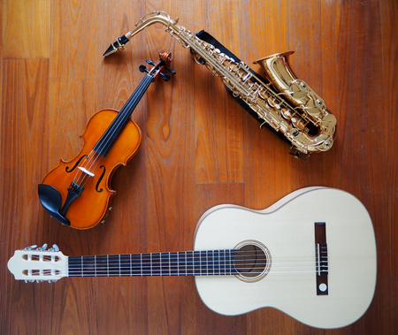 A violin, a guitar and a saxophone leaning together. Teak wood background.の写真素材