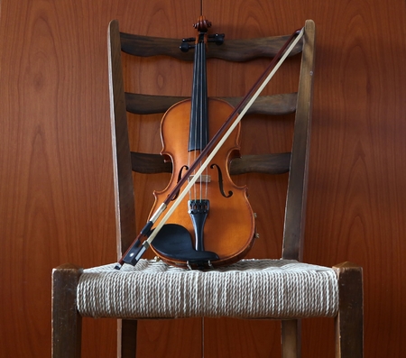 Violin with a bow on a chair. Wooden wall backgroundの写真素材