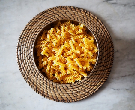 Fusilli, a type of pasta from South Italy, in a bowl on a straw round trayの写真素材