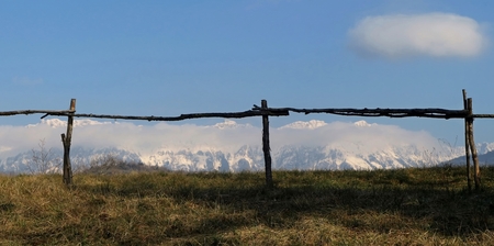Rural mountain background. Beyond the rustic wooden fence, the peaks of the Alps are covered with snow and clouds.の写真素材