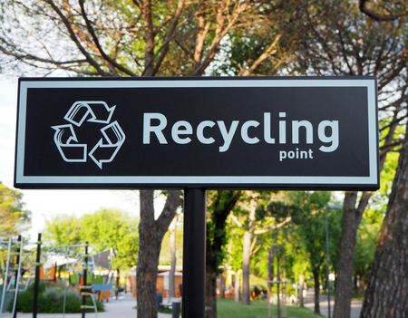 Recycling point sign, words and symbol in white color on black background. Blurred public park on behindの写真素材
