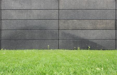 Black wall made of concrete blocks with a green meadow in front. Background for copy spaceの写真素材