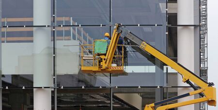 Workers on a cherry picker. They are finishing the glass facade of a building under renovationの写真素材