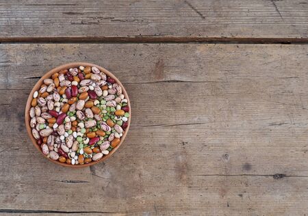 Mixture of beans varieties, azuki and green lentils in a bowl on a weathered wooden plank. Food background for copy spaceの写真素材