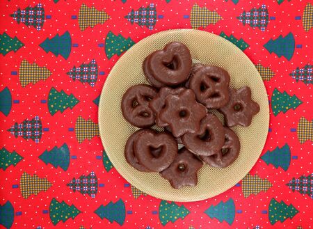 Spiced german biscuits with chocolate. In shape of pretzel, hearts and stars Christmas cookies on red tablecloth with the motif of festive trees. Background for copy space.の写真素材