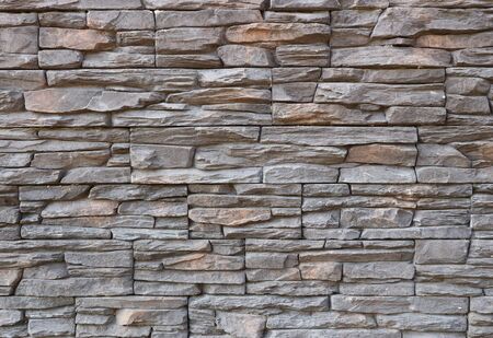 Dark gray and brown exterior wall cladding made of irregular natural stones. Stone paneling, background and texture.の写真素材