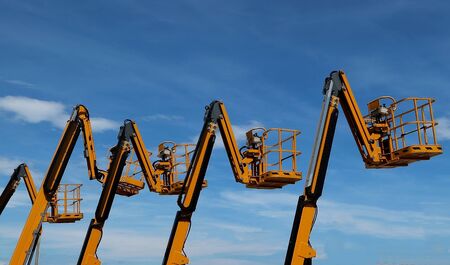 Aerial work platforms lined up against blue sky with cloudsの写真素材