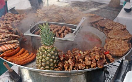 Traditional metal tray full of serbian street food. Among cevapcici, pljeskavica, various meat and boiled vegetables there is a big pineapple.の写真素材