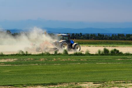 Tractor plows the field raising a large cloud of dust, after several summer days without rain