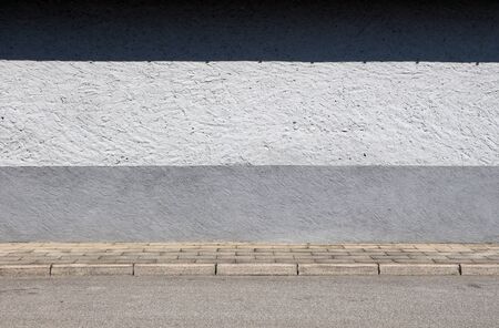 Wall painted with three horizontal stripes, one white, one black and one gray. Tiled sidewalk and an asphalt road in front. Background for copy spaceの写真素材