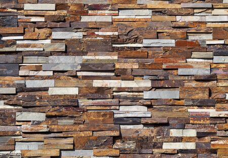Stone cladding wall made of striped stacked slabs of natural colored rocks. Panels for exterior.
