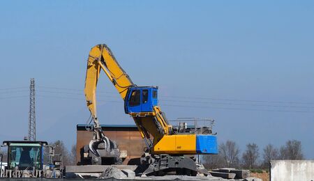 A giant excavator at work outside an industrial steel and cement areaの写真素材