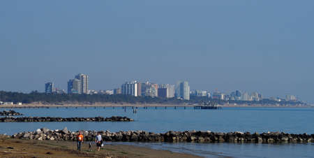 Lignano Sabbiadoro, Italy. March 3 2019. Last stretch of the beach with the skyline of the great Italian tourist center of Lignano Sabbiadoro by the North Adriatic Sea on background in early springのeditorial素材