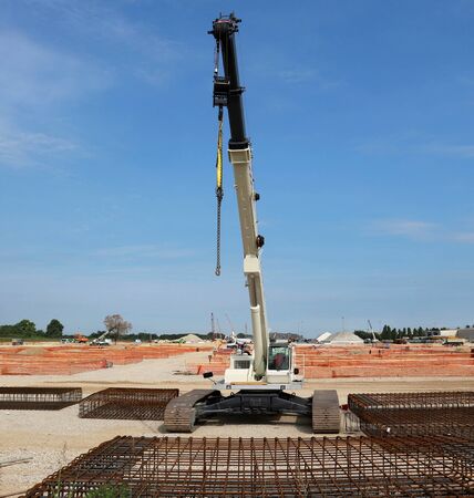 Tracked mobile telescopic crane in a large construction site, with steel cages in front and building activity behindの写真素材