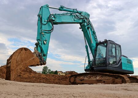 Large excavator with the scoop in the dirt, against a gray cloudy skyの写真素材