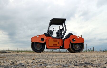 Orange paving machinery on a road under construction under a dark cloudy skyの写真素材