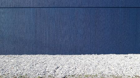 Dark blue concrete wall with white small pebbles road in front. Background for copy textの写真素材