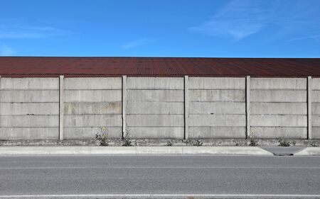 Gray concrete wall, a tin brown roof with a road in front. Urban background for copy spaceの写真素材