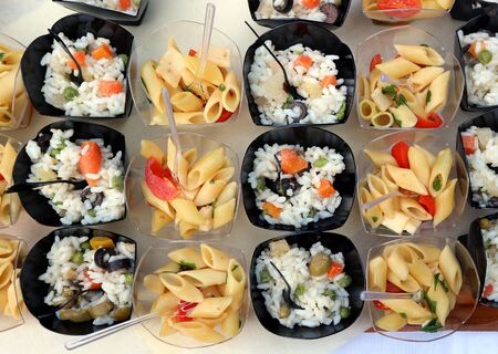Cold rice and pasta salads in small plastic containers, ready for a summer party