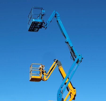 Two aerial work platforms, one over the other, against cloudless blue skyの写真素材