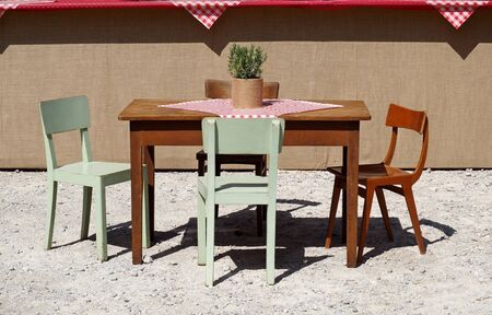 Rustic wooden table and colored chairs, with checkered tablecloth and rosemary plant, in a gravel front yard. Background for copy space,の写真素材