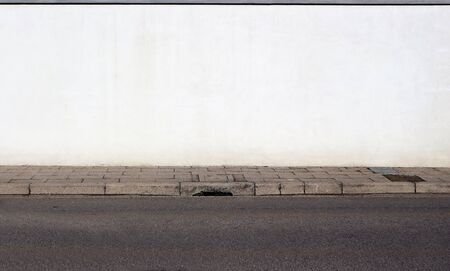 White painted wall, concrete sidewalk and an asphalt road. Background for copy space.の写真素材