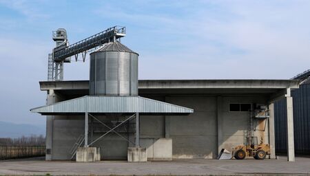 Small steel granary silo with conveyor belt in a concrete agricultural building.の写真素材
