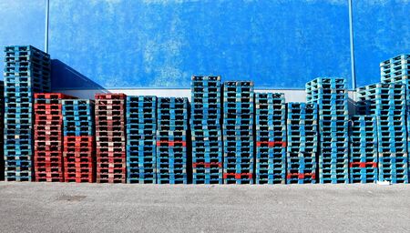 Rows of red and blue painted wooden pallets stacked against a blue wall. Asphalt road ahead. Background for copy space.の写真素材