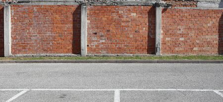 Grunge brick wall with concrete column, a strip of grass and an asphalt road in front. Background...