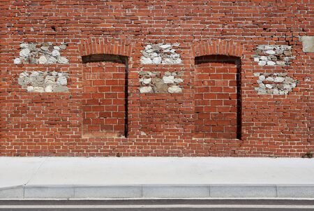 Brick wall with walled windows and natural stones insertions and a white concrete sidewalk in front. Background for copy space.の写真素材