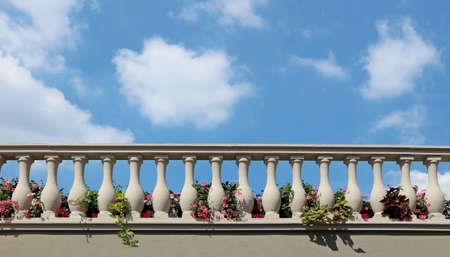 Stone balustrade of a balcony with flowers between the columns. Blue sky with fluffy clouds on background. Copy spaceの写真素材