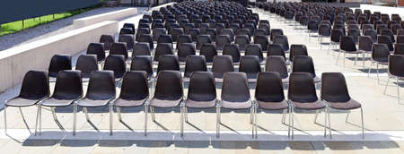Long rows of empty black plastic chairs geometrically arranged under the sun. Texture and...