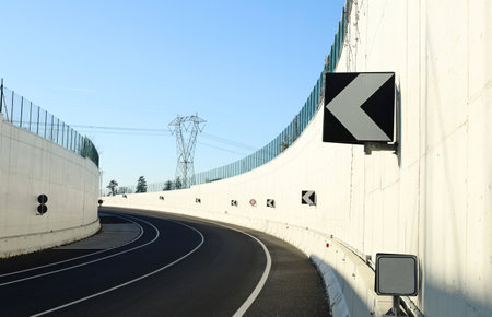 Road curve at the exit of an underpass with high white concrete wall and directional arrow signs. Background for copy spaceの写真素材