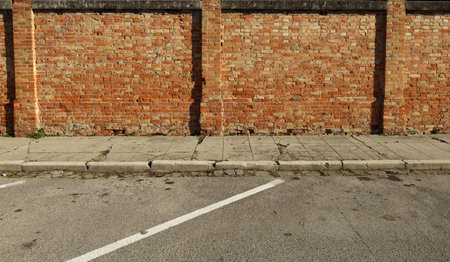 Grunge brick wall made of red and yellow bricks, a weathered sidewalk and an asphalt street....