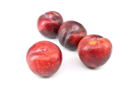 Four large red plums with little yellow dots on white backgroundの写真素材