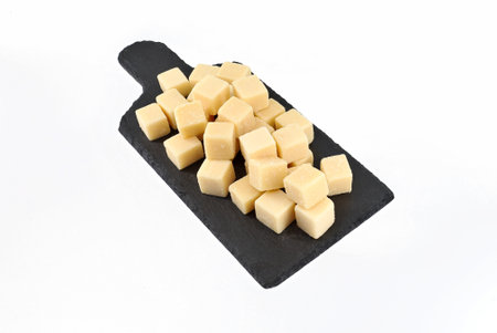 Parmesan cubes on a slate serving plate with cutting board shape. It is a hard granular cheese from North Italy. White background.の写真素材