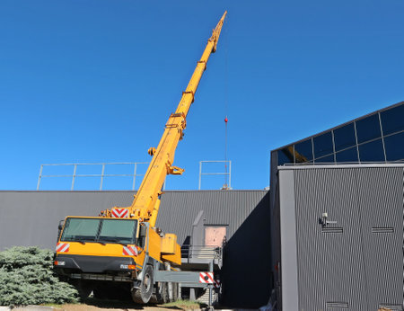 Yellow telescopic crane on a large truck working outside a modern gray buildingの写真素材