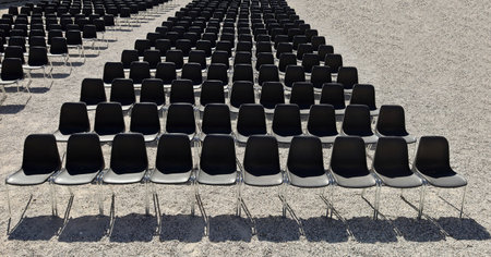 Long rows of empty black plastic chairs geometrically arranged under the sun. Textures and backgrounds. Copy space.の写真素材