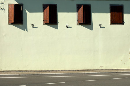 Light yellow wall with a row of old style wooden shutters in the upper side. Sidewalk and asphalt street in front. Background for copy space.の写真素材