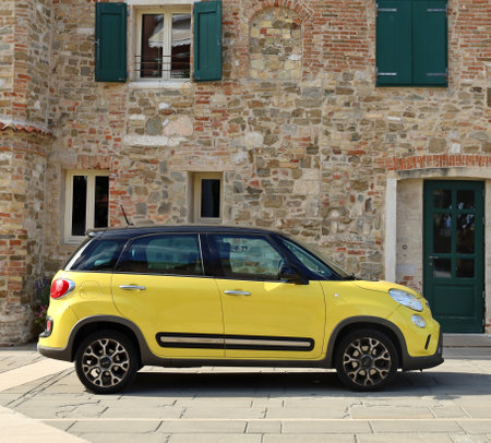 Grado, Italy. August 17, 2021. Yellow Fiat 500 L, five door compact minivan, parked on a road side of the old quarter.のeditorial素材