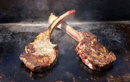Two crossed tomahawk steaks cooked on a metal grill.の写真素材