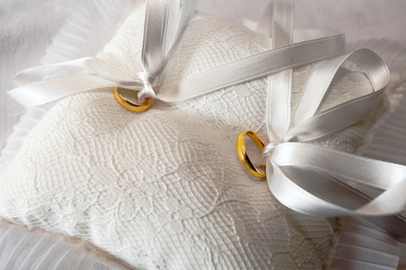 yellow gold wedding rings on white pillow with tasselsの写真素材