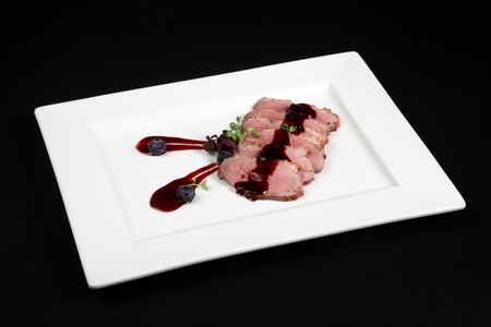 duck meat with cranberry cream in white plate on a black backgroundの写真素材