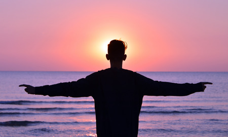 a boy standing on the beach while the sun rises, backlighting