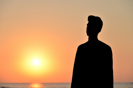 a boy standing on the beach while the sun rises, backlightingの写真素材