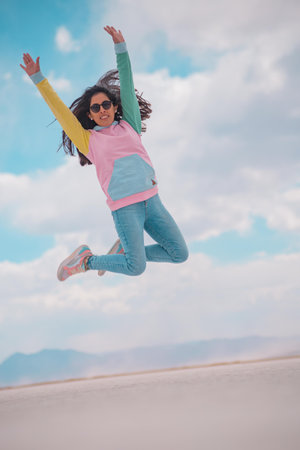 Young woman jumping and playing in a salt lake, with celestial sky and radiant sunの写真素材